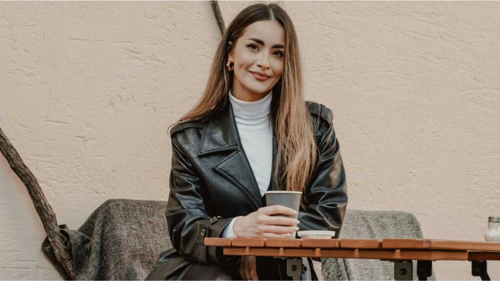 Nasmijana žena sjedi sama na kavi u kafiću i pokazuje kako povećati samopouzdanje kroz samostalne aktivnosti.