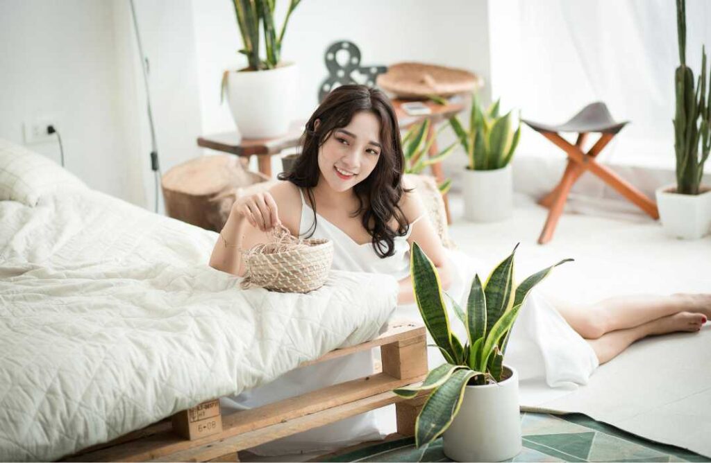 Mlada žena opušteno sjedi uz biljku, ilustrirajući kako biljke za spavaću sobu poboljšavaju zrak i san.