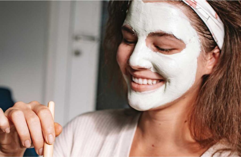 3 prirodna načina kako učinkovito umanjiti vidljivost proširenih pora Nasmijana mlada žena s nanesenom maskom od gline na licu kako bi riješila proširene pore.