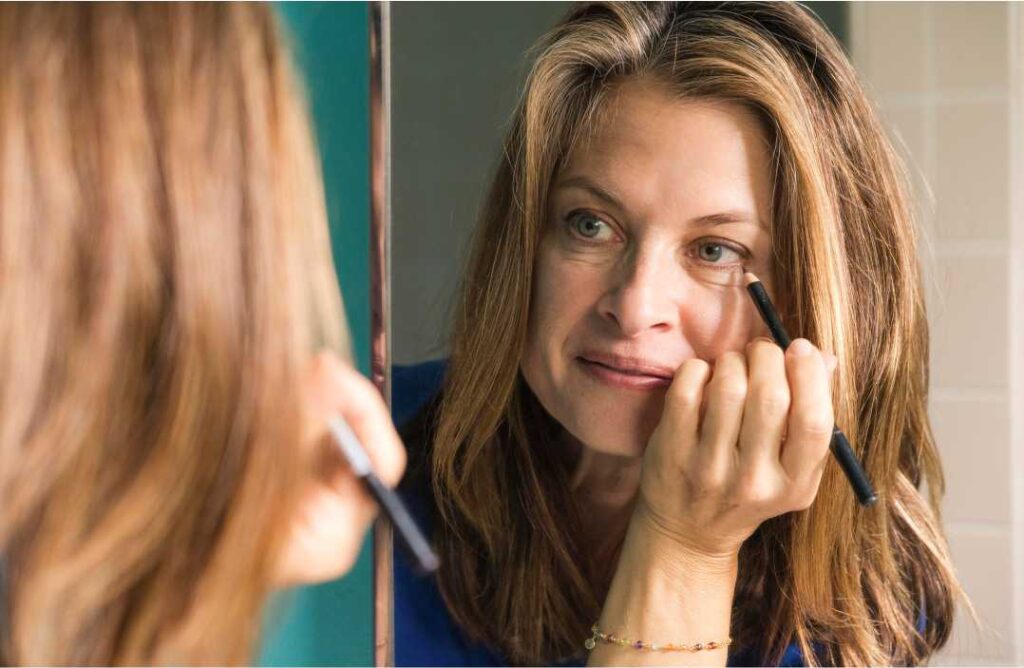 Žena u ogledalu gleda umorno lice i kako ukloniti podočnjake.