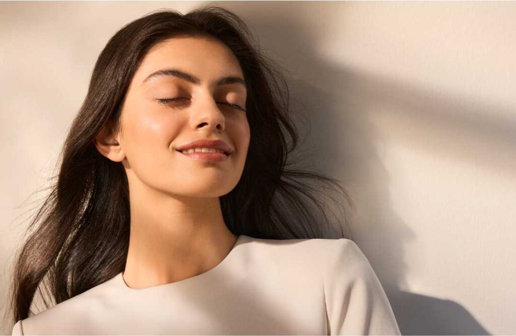 Krupni plan nasmijane mlade žene zatvorenih očiju koja uživa u sunčevoj svjetlosti, pokazujući zdravu, mat i zaštićenu kožu lica, što ilustrira učinkovitost Eucerin Oil Control zaštite od sunca.