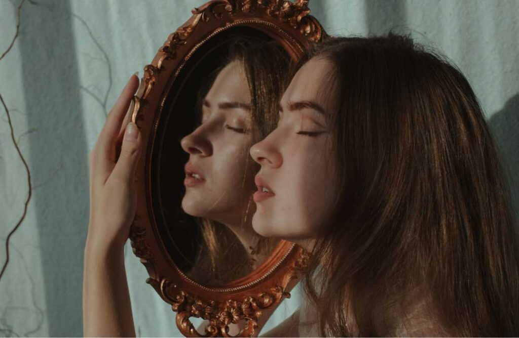 Zamišljena žena gleda u dva odraza u starinskom ogledalu, vizualizirajući nesvjesne procese i pitanje kako biramo partnere na temelju prošlosti.