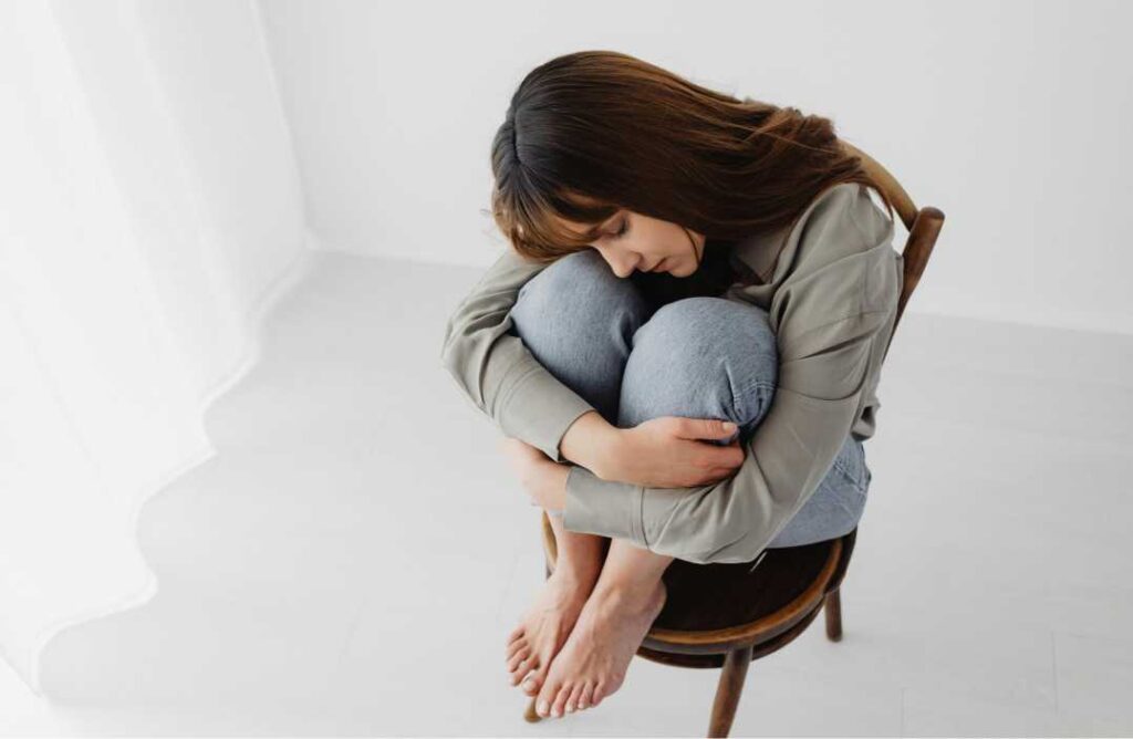 Uznemirena žena u fetalnom položaju na stolici, što prikazuje suptilne simptome psihoze i utjecaj THC-a na psihu, a dio je analize o temi kanabis i psihoza.