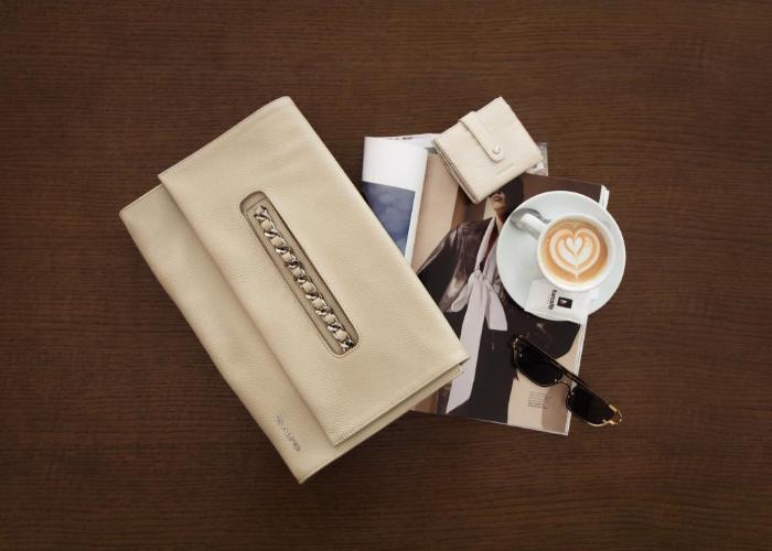 Galko torbe u modnoj flat lay kompoziciji: krem kožna pismo torba s metalnim detaljem, mali novčanik, otvoreni modni časopis, sunčane naočale i šalica kave s latte artom na tamnoj drvenoj površini.