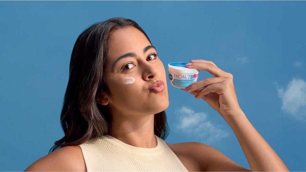 NIVEA FACIAL – ultra lagana hidratantna njega za sve potrebe kože Mlada žena s malo kreme na obrazu drži u ruci teglicu NIVEA FACIAL hidratantne kreme ispred plave pozadine s oblacima.