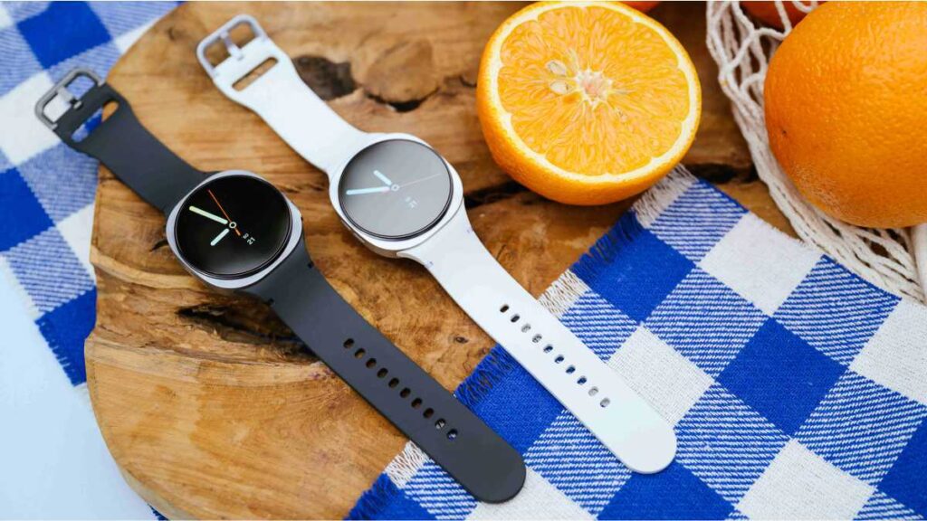 Zašto umor ne bi smio biti dio svakodnevice Crni i bijeli Samsung Galaxy Watch pametni satovi položeni na drvenu podlogu uz svježe naranče.
