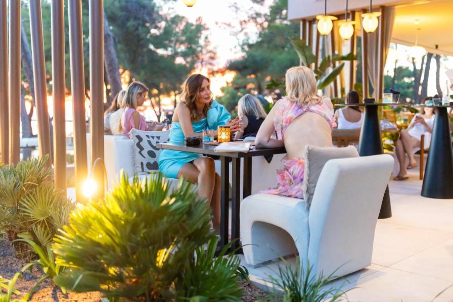 Antonija i Edita sjede i razgovaraju za stolom na otvorenoj terasi mediteranskog lounge bara.