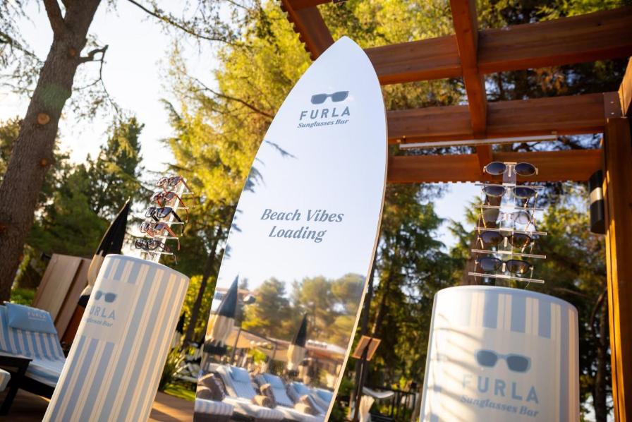 Pogled odozgo na personalizirane ležaljke s logotipom 'Furla Sunglasses Bar' uz bazen.