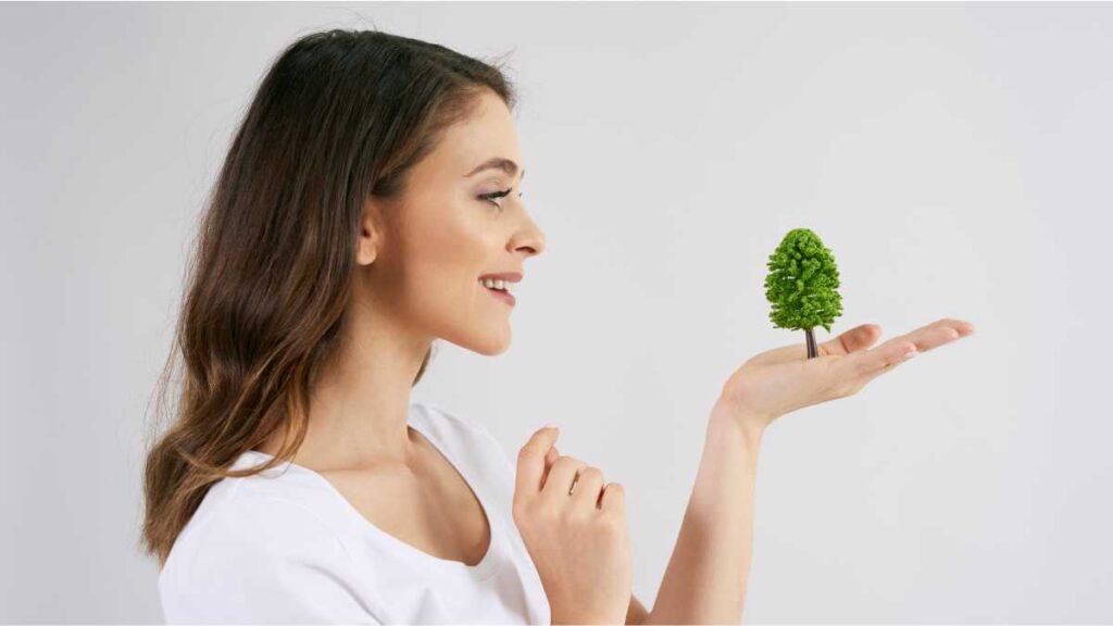 Promocija projekata s misijom: Kako komunicirati održivost bez greenwashinga Žena drži malu maketu drveta na dlanu - kako komunicirati održivost i ekološku osviještenost brenda.