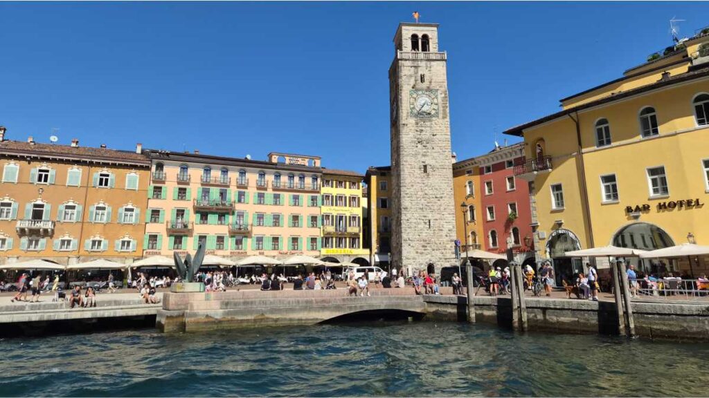 Riva del Garda: Između moćnih Alpa, tirkiznog jezera i talijanskog hedonizma Riva del Garda na jezeru Garda, Italija: živahna luka i srednjovjekovni toranj Apponale u povijesnoj jezgri grada na sunčan dan.