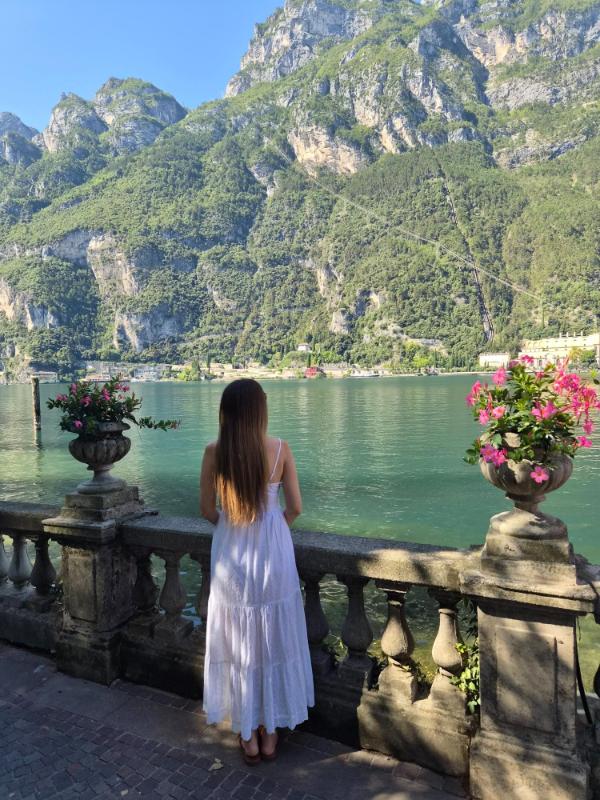 Urednica i influencerica Marijana Glavaš u bijeloj haljini gleda na jezero Garda i Alpe s kamene šetnice u Riva del Gardi.