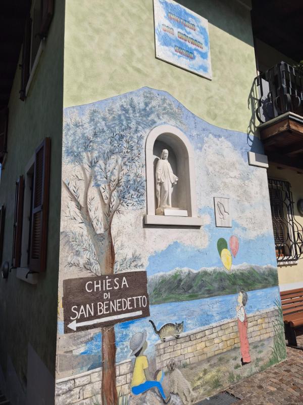 Živopisni mural na fasadi zgrade u Limone sul Garda s putokazom za crkvu San Benedetto i kipom Bogorodice.