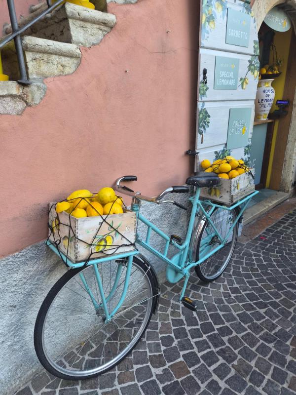 Retro plavi bicikl parkiran ispred trgovine u Limone sul Garda s drvenim gajbama punim žutih limuna na prednjem i stražnjem nosaču.