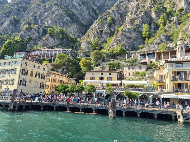 Pogled s broda na šarene kuće i hotele uz obalu Limone sul Garda stisnute pod strmim alpskim planinama.