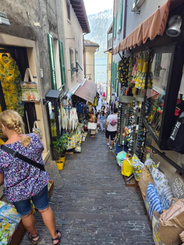 Uska uličica sa stepenicama i trgovinama prepunima šarenih haljina s motivima limuna, torbi i suvenira u Limone sul Garda.