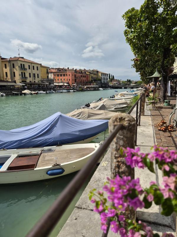 Pogled na Canale di Mezzo u Peschieri del Garda s usidrenim čamcima, povijesnom arhitekturom i cvijećem u prvom planu.