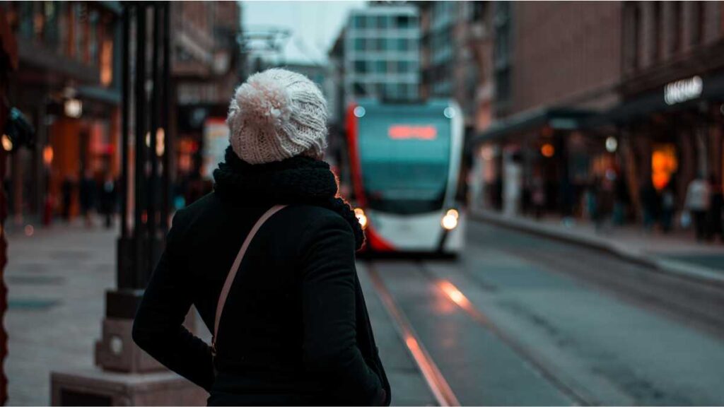 Žena na stanici čeka dolazak tramvaja u sumrak – Priča o odgađanju života.